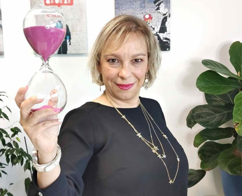 A woman holding an hourglass with a pink liquid.